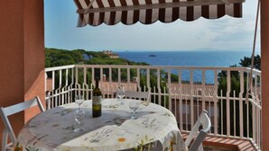 A balcony with a table set for two, a bottle of wine, and a view of the sea and hills. - Mimose 2 by Interhome (Rio Marina)