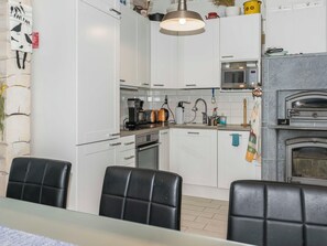 A modern kitchen with white cabinets, a built-in oven, a microwave, and a pizza oven. There are black chairs around a table, and a hanging light fixture above.