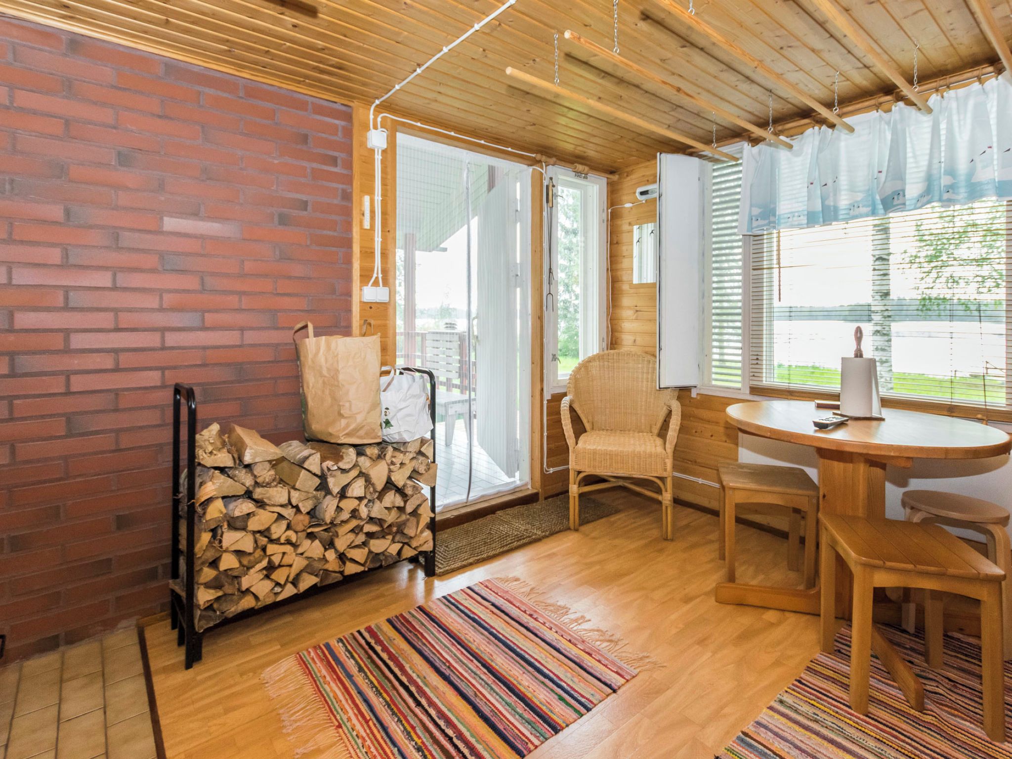 A cozy room with a brick wall, a wooden ceiling, a wicker chair, a small table, and a window with blinds.