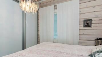 A bedroom with a large bed, a chandelier, wooden panel walls, and a window with blinds.