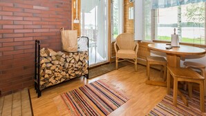 A cozy room with a brick wall, a wooden ceiling, a wicker chair, a small table, and a pile of firewood.