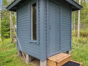 A small, single-story cabin with a window and a door, surrounded by greenery.
