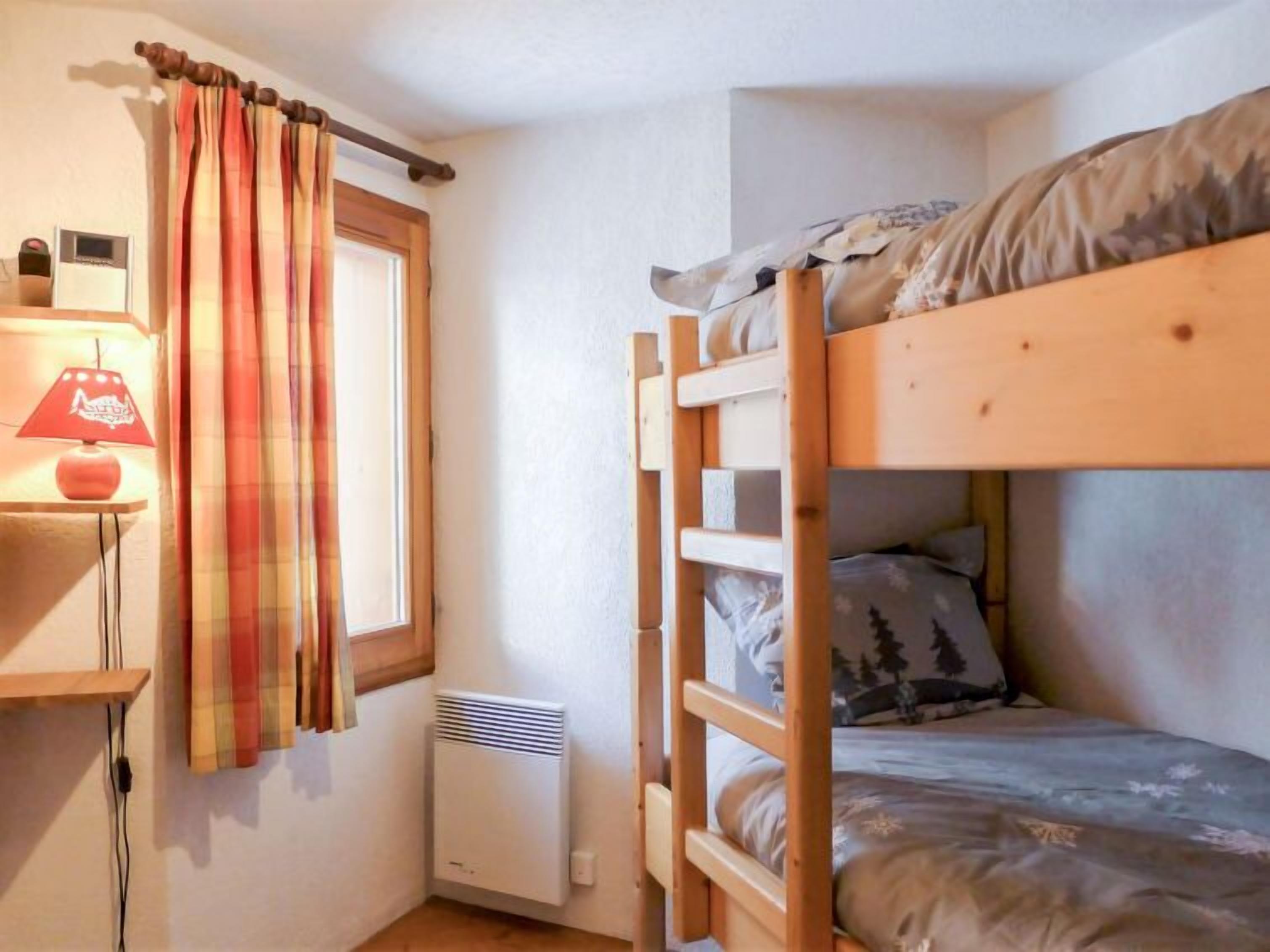 A bunk bed room with a window, a heater, and a lamp on a bedside table.