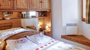 Une chambre à coucher avec des armoires en bois, un lit avec une literie à motifs, une table de chevet avec une lampe et une fenêtre avec des rideaux.