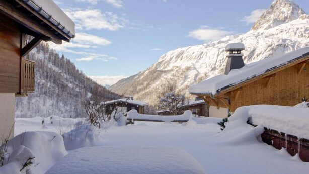 Un village de montagne enneigé, avec des bâtiments en bois et un sommet imposant qui se détache à l’arrière-plan.