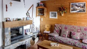 Un salon chaleureux avec une cheminée en pierre, des murs en bois, un canapé agrémenté de coussins à motifs et une petite table.