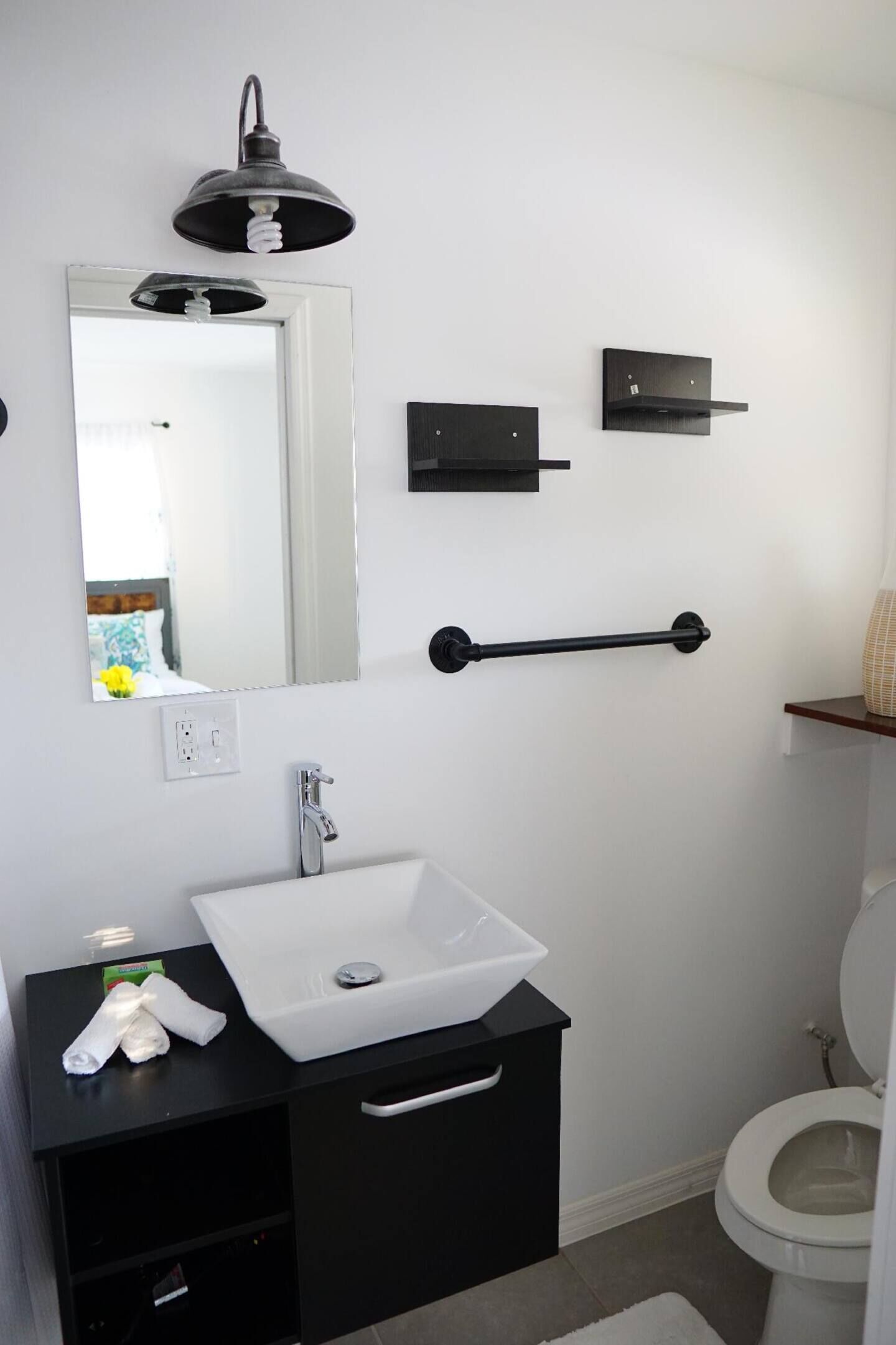 A modern bathroom with a white sink, black vanity, a mirror, a towel rack, and a toilet.