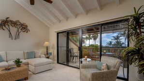 A spacious living area with a large sliding glass door leading to an outdoor balcony with a view of palm trees. - Ocean-View 2BR Maui Condo with Lanai, Steps from the Beach (Kihei)