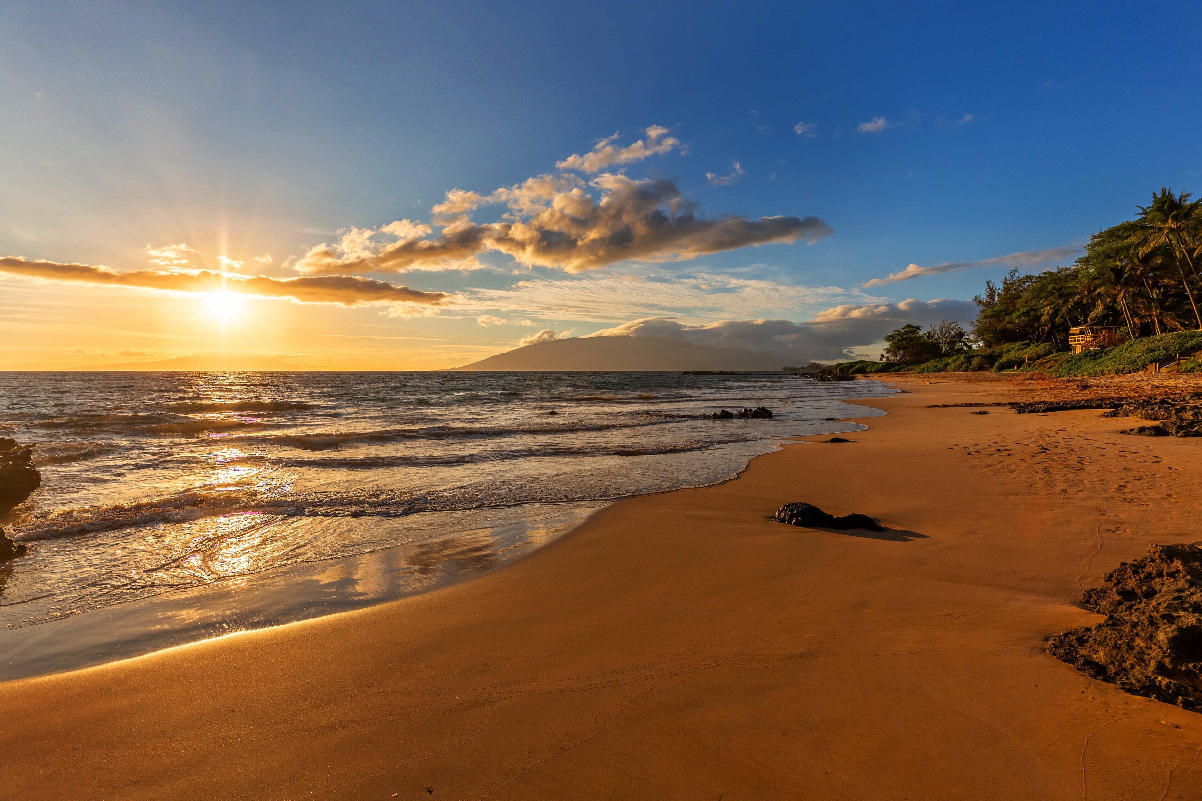 Ein Strand mit blauem Himmel, Meereswellen und einem fernen Berg.