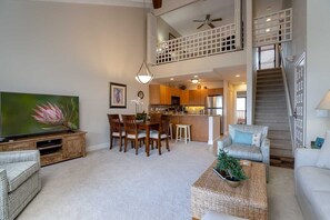 A spacious living area with a dining table, chairs, a sofa, a TV, and a staircase leading to an upper level.