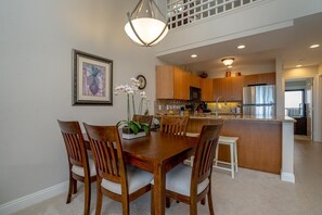 A modern kitchen with wooden cabinets, a stainless steel refrigerator, and a dining area with a wooden table and chairs.