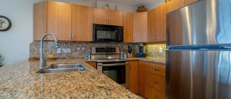 A modern kitchen with granite countertops, stainless steel appliances, wooden cabinets, and a built-in microwave.