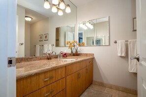Un baño con encimera de granito, armarios de madera, un espejo grande y un lavamanos.