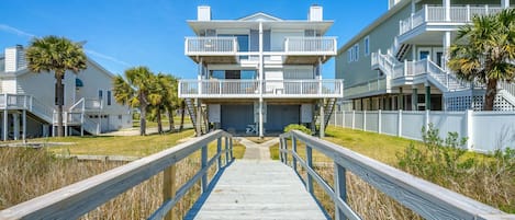 A beachfront property with a wooden boardwalk leading to a multi-story building with balconies.