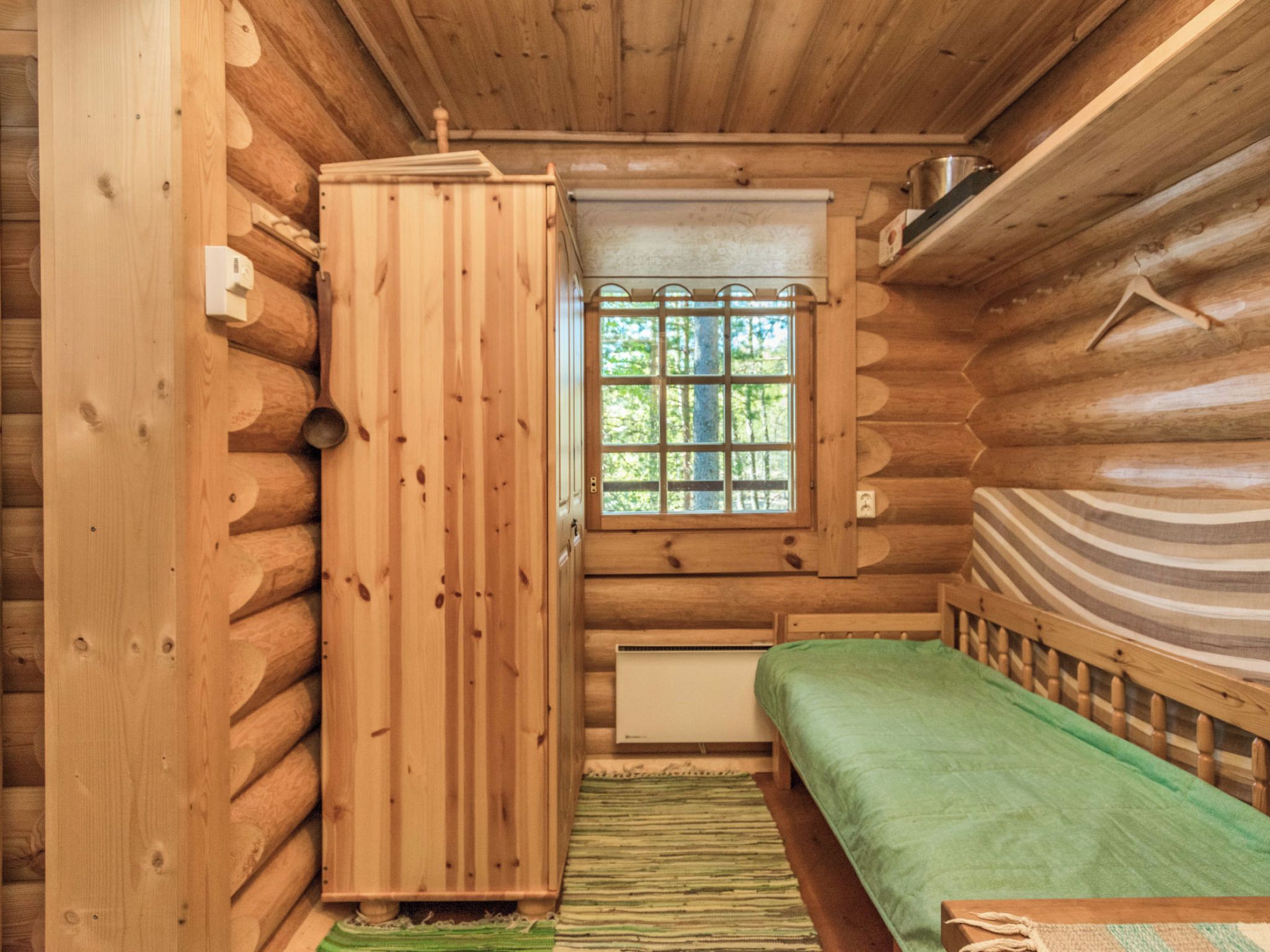 Habitación tipo cabaña de troncos con cama, ventana con barrotes y radiador.