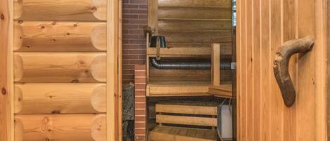 A wooden cabin interior with a fireplace, a brick wall, and a wooden bench.