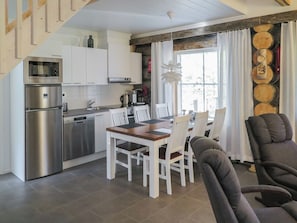 A modern kitchen with stainless steel appliances, a dining area with a wooden table and white chairs, and a large window with curtains.