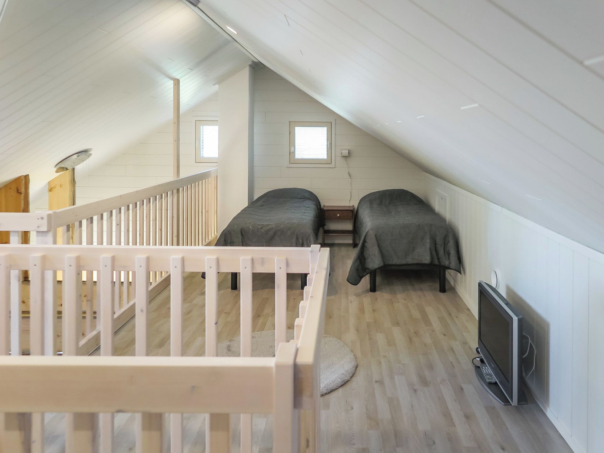 A high-ceilinged room with two beds, a TV, and a small window.