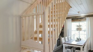 A wooden staircase leading to a dining area with a table and chairs, a television, and a window with curtains.