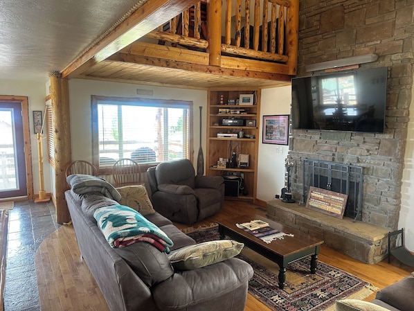 A cozy living room with a stone fireplace, a television mounted above it, a comfortable sofa, and a wooden bookshelf.