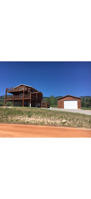 A wooden cabin with a garage, surrounded by a grassy area and hills.