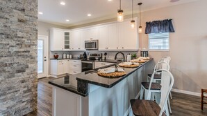 A modern kitchen with white cabinets, a central island, and pendant lighting. - Experience the Captain's Quarters.  A Historic 1920 American Four Square. (Tarpon Springs)