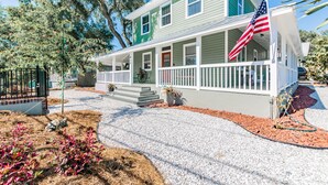 A two-story house with a porch, an American flag, and a well-maintained garden. - Experience the Captain's Quarters.  A Historic 1920 American Four Square. (Tarpon Springs)