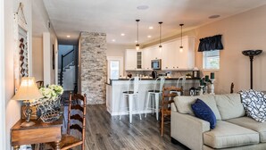 A modern kitchen with white cabinets, a central island with bar stools, and pendant lighting. - Experience the Captain's Quarters.  A Historic 1920 American Four Square. (Tarpon Springs)