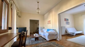 A spacious living room with a wooden dining table, a sofa, a lounge chair, and a patterned rug. - Sunny Apartment (90m2) in Athens center (Athens)