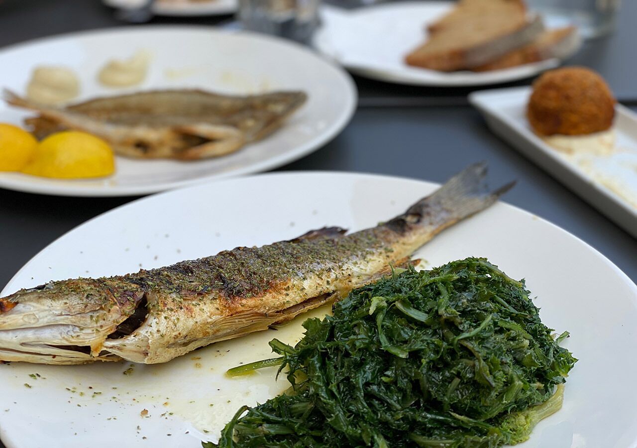 Prato com um peixe inteiro, vegetais e fatias de limão.
