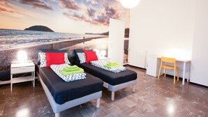 A room with two beds, a desk, and a large mural of a beach scene.