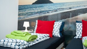 A bedroom with a bed, pillows, a lamp, and a view of the ocean.