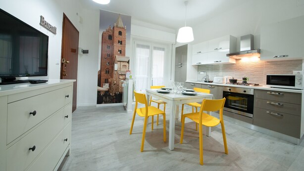 A modern kitchen with white cabinets, a built-in oven, and a dining area with yellow chairs.