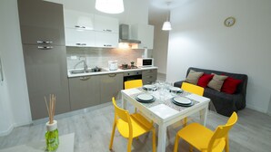 A modern kitchen with white cabinets, a dining table set with yellow chairs, and a grey sofa with red cushions.