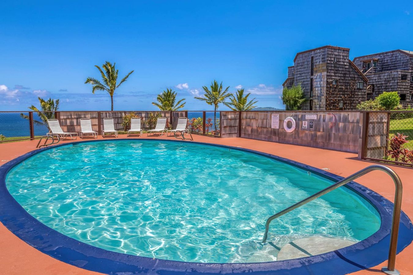 A pool with clear blue water, surrounded by lounge chairs and a fence.