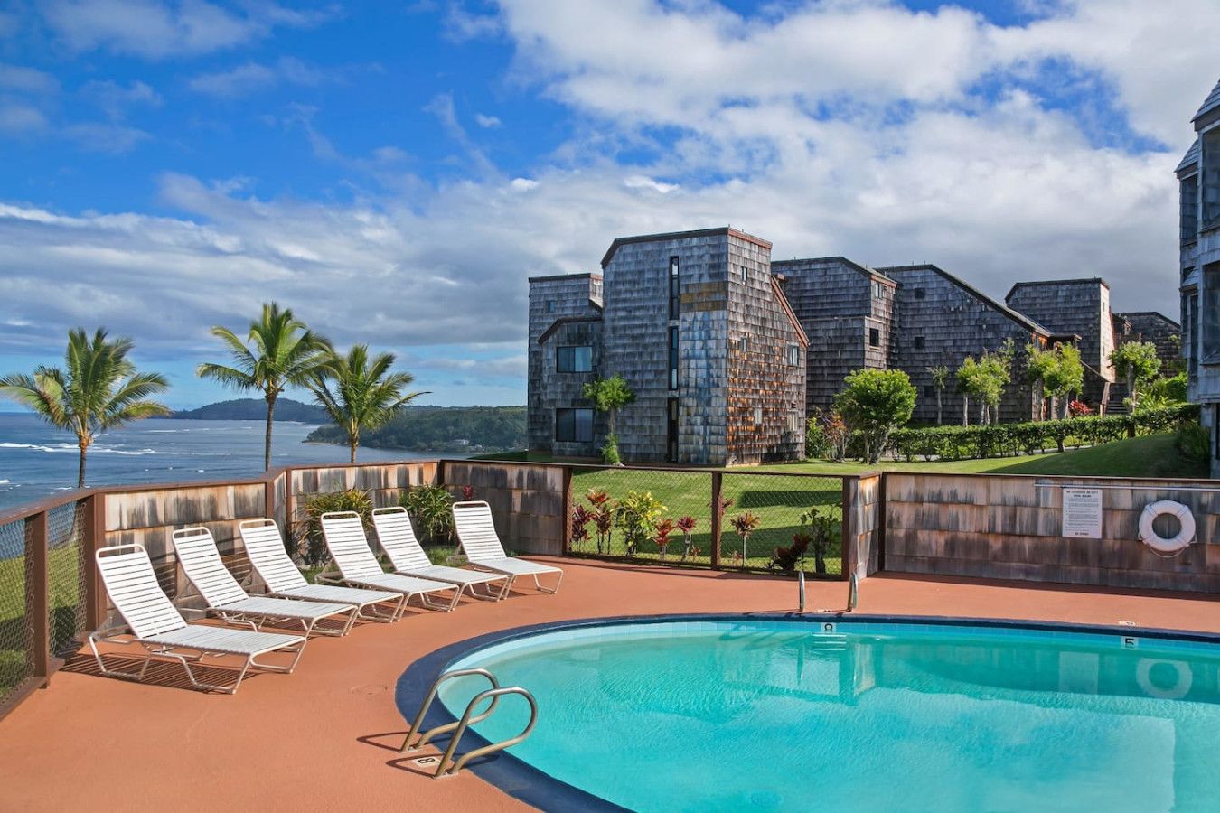 A poolside area with lounge chairs, a clear blue pool, and a view of a stone building with a landscaped garden.