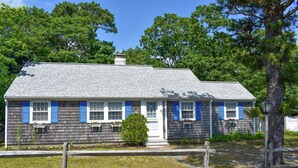 A two-story house with a grey shingled roof, white trim, and blue shutters. - Neat, clean and affordable 4 bedroom home with central air in West Dennis (West Dennis)