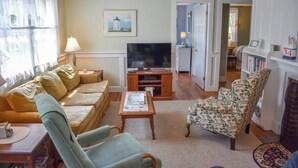 A living room with a sofa, armchair, TV, and bookshelf. - Neat, clean and affordable 4 bedroom home with central air in West Dennis (West Dennis)