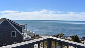 Una terraza de madera con vistas a una playa, con una casa al frente.