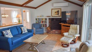 Una sala de estar con un sofá azul, una mesa de centro de madera, un sillón estampado y un sillón color beige, además de una chimenea.