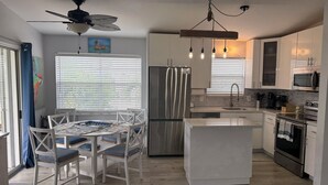 A modern kitchen with a central island, stainless steel appliances, and a dining area with white chairs.
