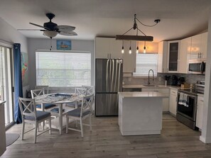 Una cocina moderna con una isla central, electrodomésticos de acero inoxidable y un comedor con sillas blancas.