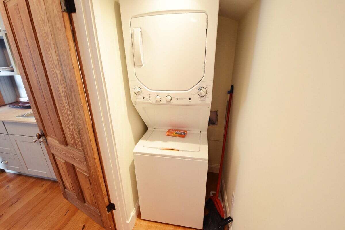 A compact washer and dryer unit in a small room with wooden flooring and a door.