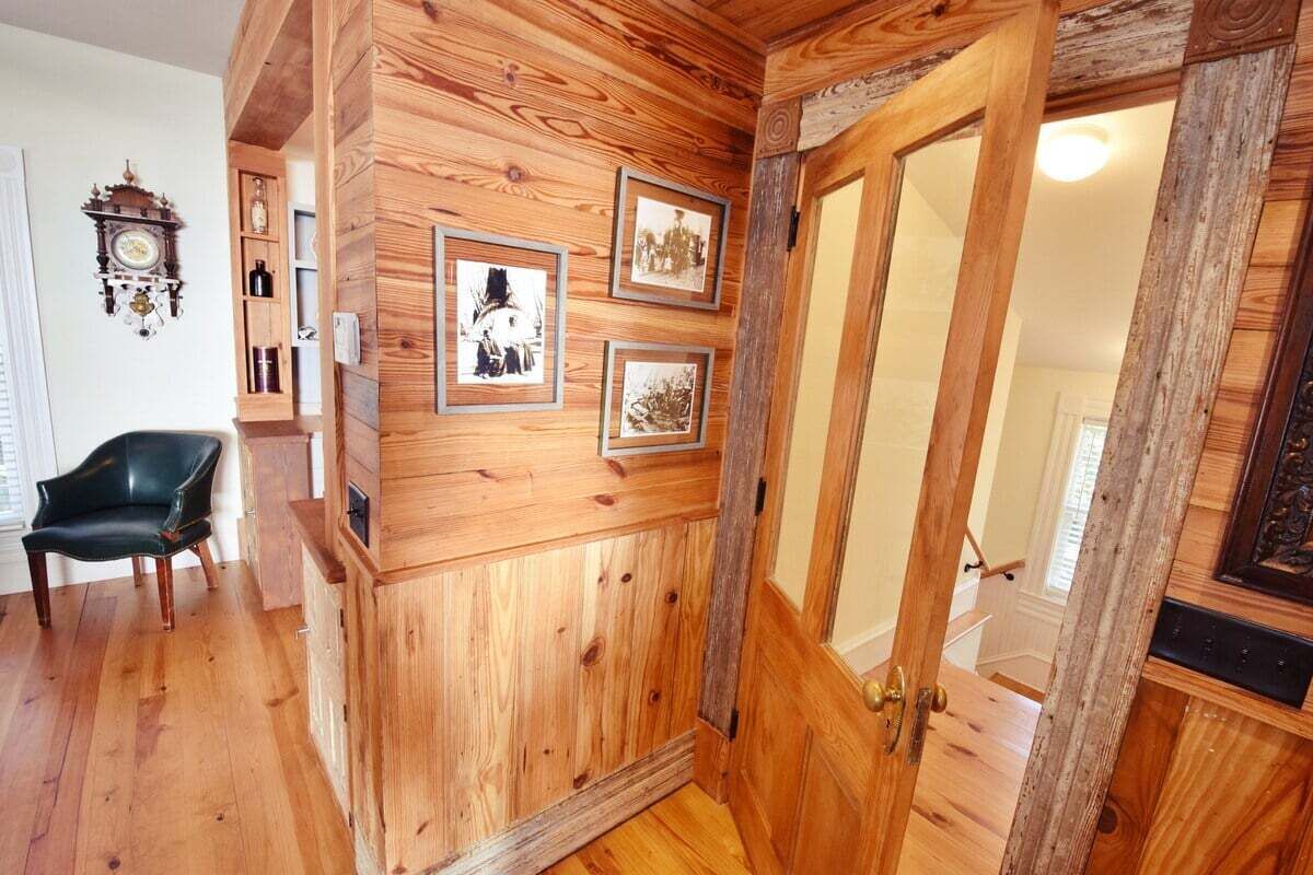 Una habitación con paneles de madera, una puerta, un sillón de cuero negro y cuadros enmarcados en la pared.