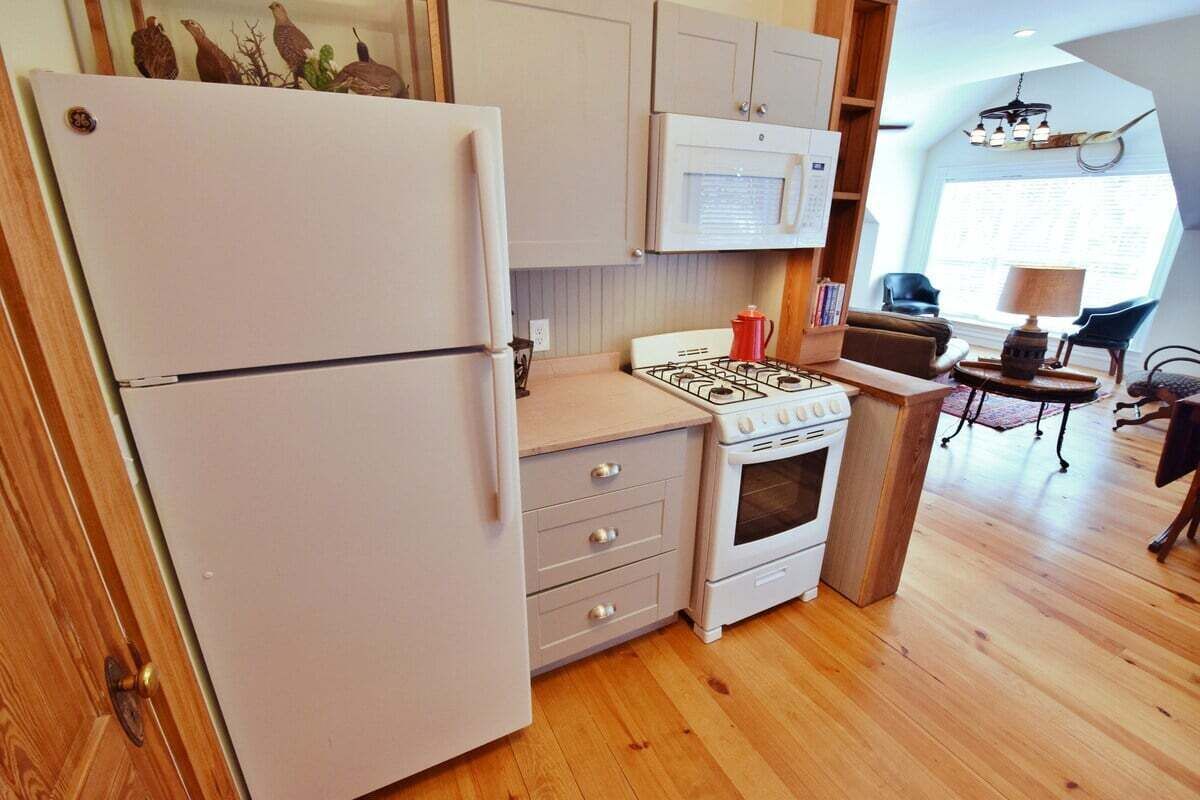 A compact kitchen with a refrigerator, stove, microwave, and wooden cabinets.