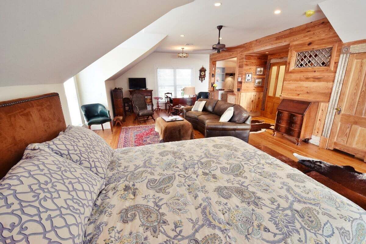 A cozy loft bedroom with a large bed, a seating area with a sofa and chairs, a fireplace, and wooden walls.