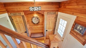 Un interior de madera con una escalera, puertas de madera, un espejo y un cuadro en la pared.