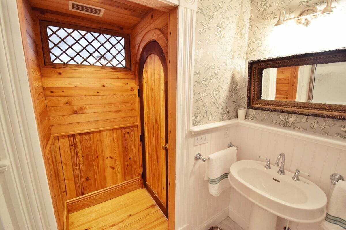 Une salle de bain aux murs lambrissés, dotée d’un grand miroir, d’un lavabo et de toilettes.