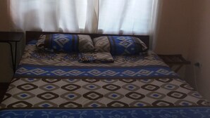Un lit avec une literie à motifs, une table de chevet et une fenêtre ornée de rideaux légers.