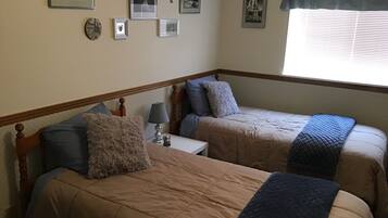 A bedroom with two beds, a nightstand, a lamp, and a window with blinds.